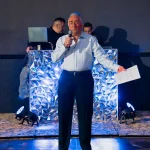 Alberto ofreciendo discurso en su celebración de 75 años, fotografía profesional de evento social en salón con iluminación ambiental.