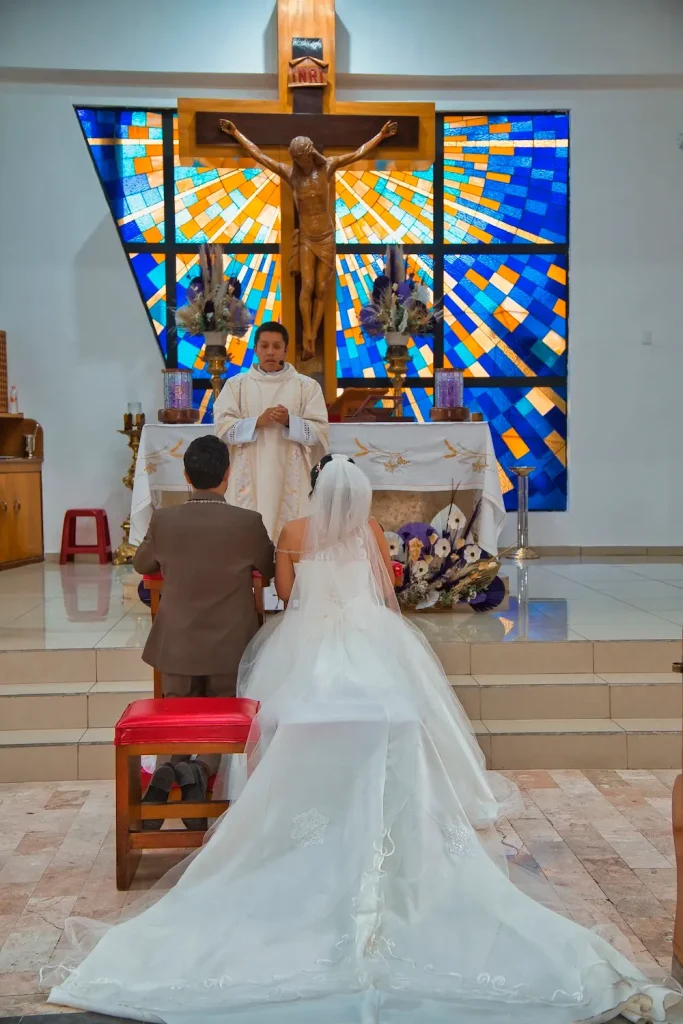 Pareja frente al altar bajo crucifijo iluminado en ceremonia religiosa de boda.