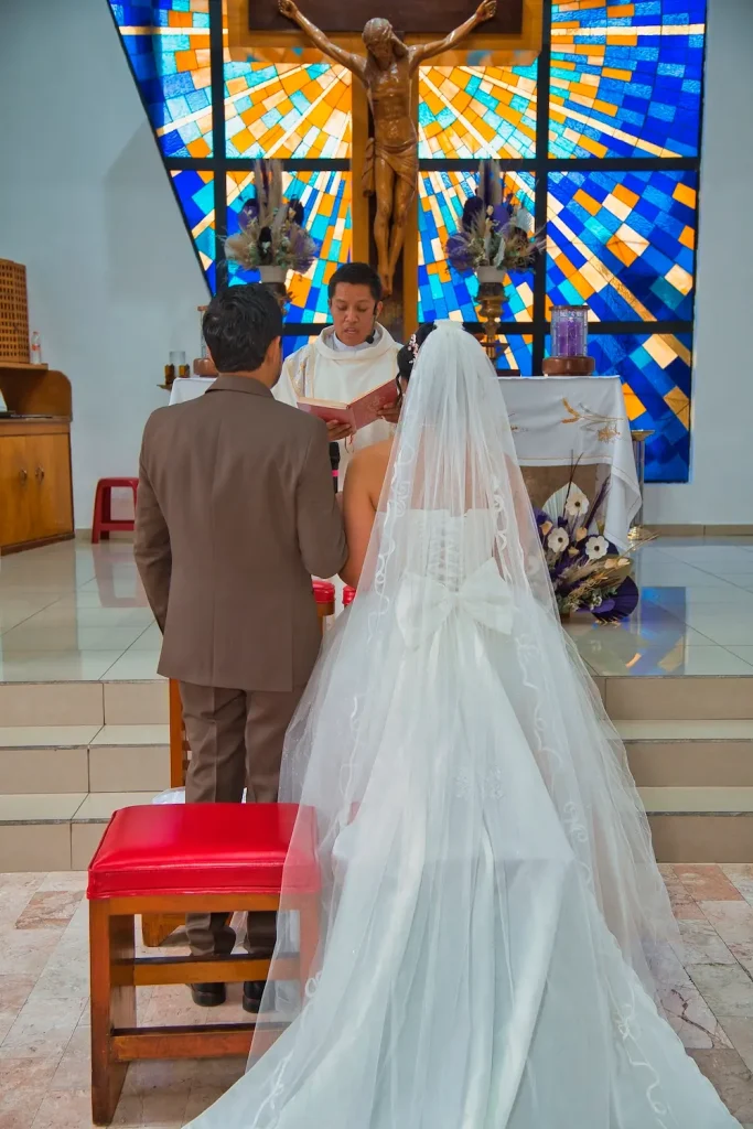 Entrada de la novia al altar acompañada del novio en boda religiosa con vitrales de fondo.